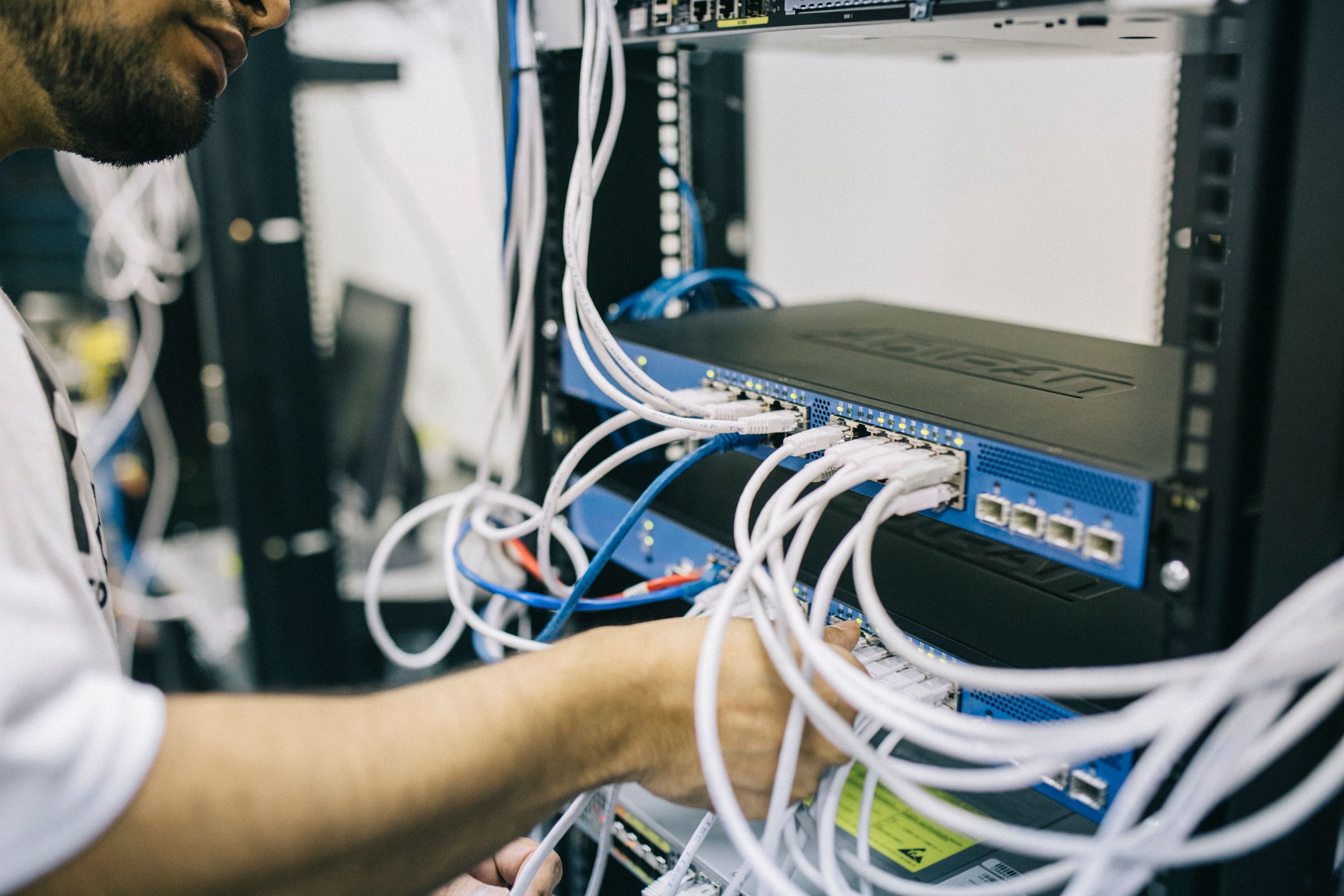An engineer connecting network cables to a switch in a server rack
